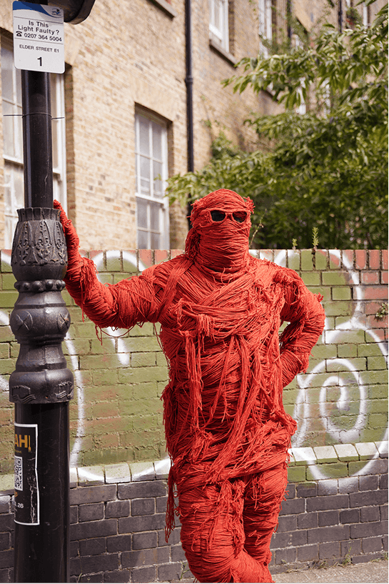 Fred, StrategiQ's mascot, wrapped in orange thread, standing by a lamppost
