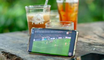 A football game on a phone screen surrounded by drinks on a summer day